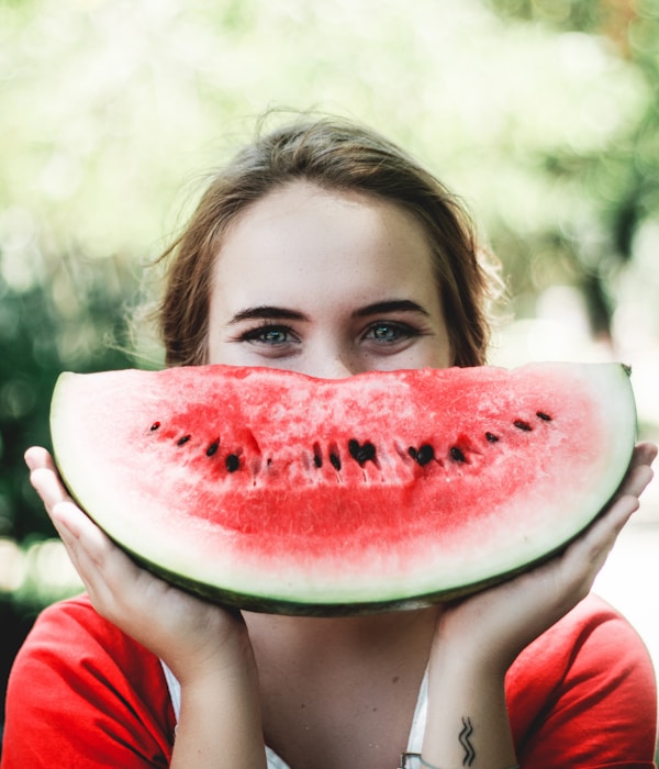 Smiling woman playfully holding up a slice of watermelon like a grin in front of her face